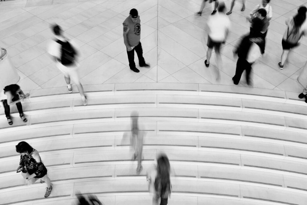 Black and white photo of a lone man standing still among blurred crowds in a public space, symbolizing identity vulnerability and unnoticed threats.